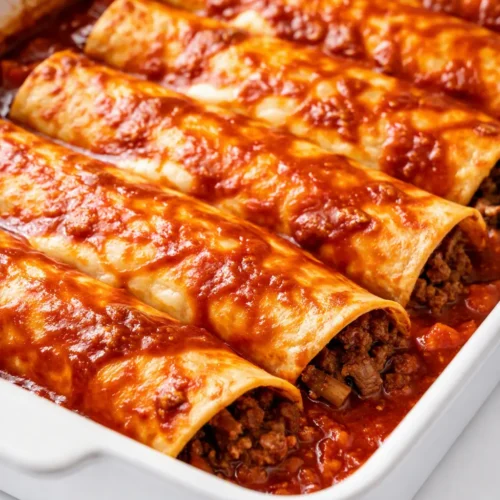 Ground beef enchiladas with bubbly melted cheese, rich red sauce, and golden-brown edges, garnished with fresh cilantro.
