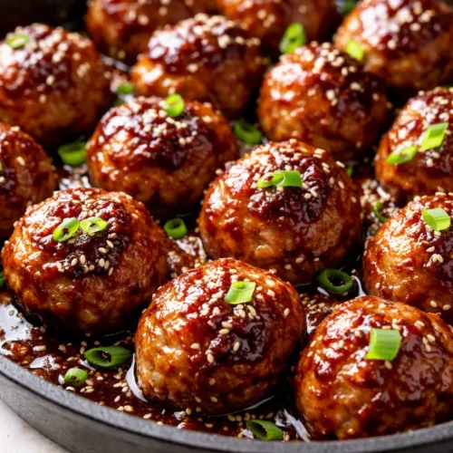 Sticky, caramelized honey garlic meatballs glistening in a bowl, topped with sesame seeds and scallions.