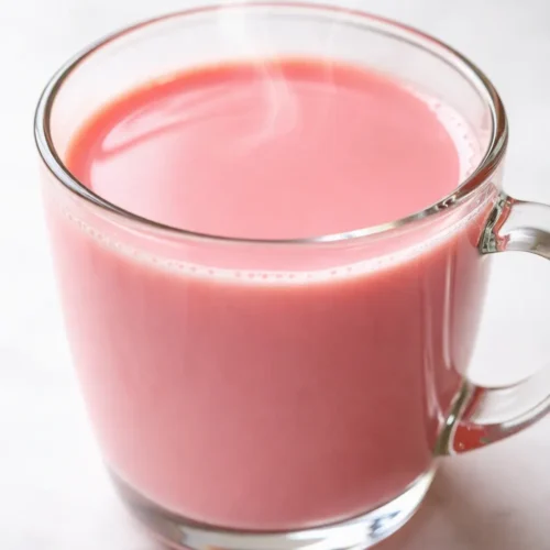 Vibrant pink Kashmiri noon chai in a clear glass topped with crushed pistachios and a creamy frothy layer