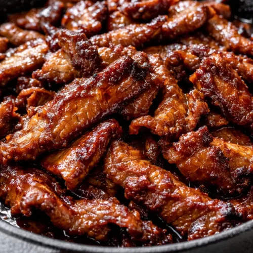 Glossy Korean beef bulgogi strips sizzling in a pan with sesame seeds and green onions, tender and caramelized.