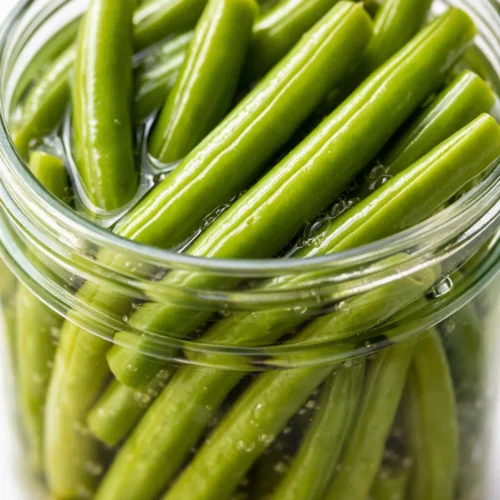Glass jar of crisp, tangy pickled green beans with garlic and dill, showing their vibrant green color and crunchy texture.