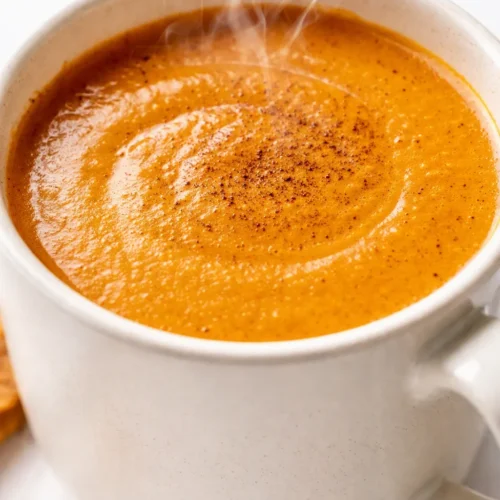 Creamy pumpkin spice latte in a ceramic mug with velvety milk foam, cinnamon dusting, and warm orange-brown tones.